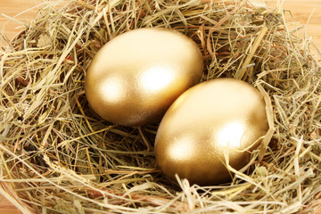 Naklejka na ściany i meble Three golden hen's eggs in the grassy nest on the wooden table