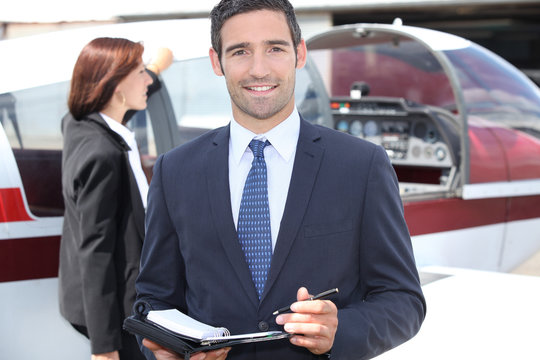 Man in suit taking notes in front of an airplane