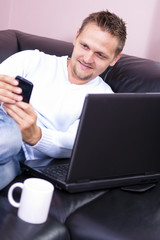 Men sofa with phone and computer use.