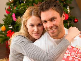 Young couple with gifts in front of Christmas tree