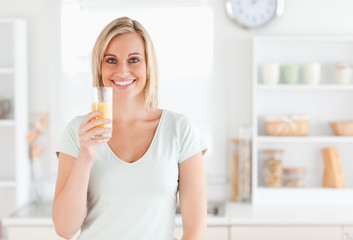 Charming woman holding glass filled with orange juice while stan