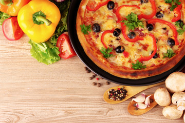 tasty pizza on the plate and vegetables on a wooden background