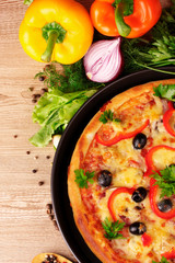 tasty pizza on the plate and vegetables on a wooden background