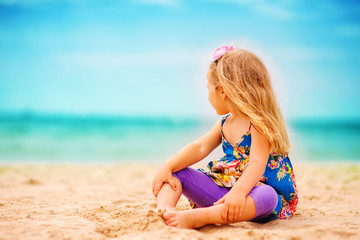 stylish toddler girl sit on sandy exotic beach