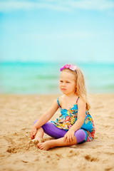 stylish toddler girl sit on sandy exotic beach