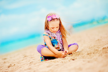stylish toddler girl sit on sandy exotic beach