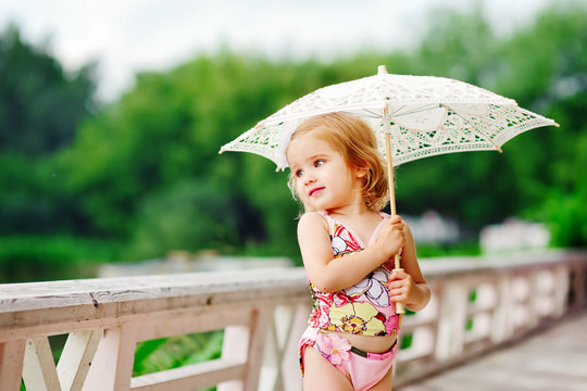 cute little girl in swimsuit with sun umbrella taking sunbathe