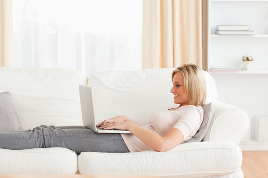 Woman using a laptop while lying on a sofa