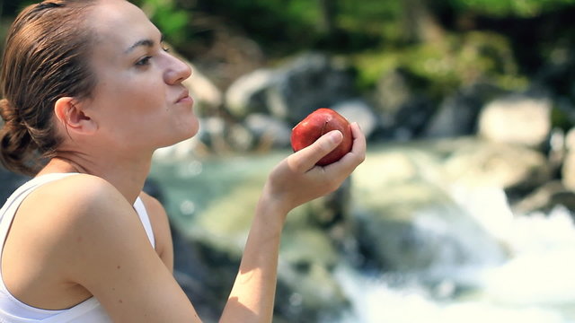 Young woman eats fresh apple, outdoors