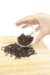 pouring pepper, hand pouring bleack pepper from clear cup.