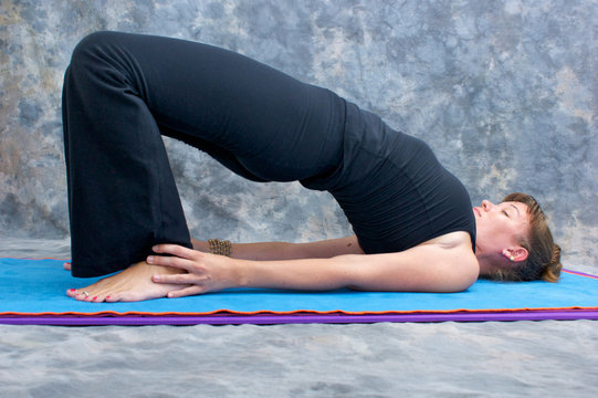 young woman doing yoga exercise on mat in Setu Bandhasanasana or