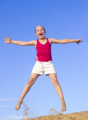 Fototapeta premium Little joyful girl jumps against blue sky