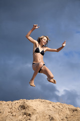 Young girl in swimsuit jumps above the sands embankment