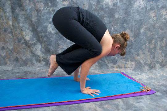 woman balancing on mat in studio doing yoga posture Bakasana or