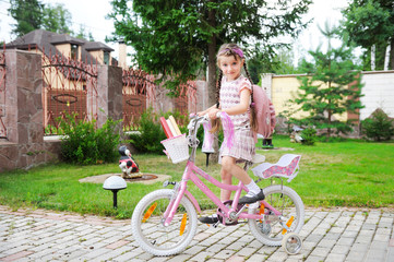 Young school girl with bagpack rides her pink bike to school
