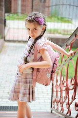 Young school girl with pink bagpack waits standing on stairs