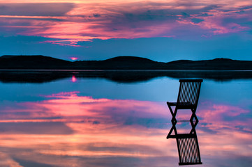 Scenic view of sunset over inlet and hills with a chair in the c