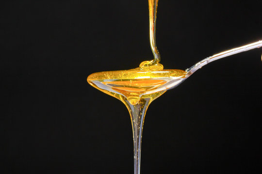 tasty honey in spoon on black background