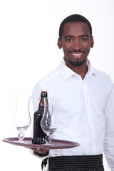 Black waiter carrying bottle of beer on tray