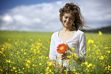 Naklejka na ściany i meble Woman with red flowers in rapeseed field.