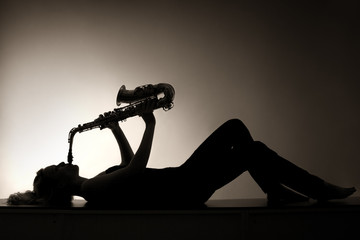 Silhouette of lying woman playing saxophone, sepia toned.