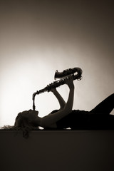 Silhouette of woman playing saxophone, sepia toned.