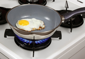 Fried egg in teflon pan on the gas stove.
