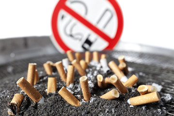 Cigarette stubs in ash with no smoking sign.