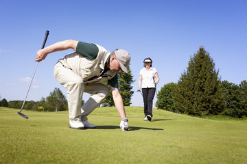 Obraz premium Golf player couple on green picking ball.