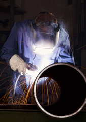 Worker welding pipe in workshop.