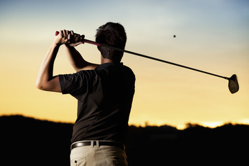 Golfer teeing off at sunset.