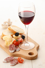 Wineglass with red wine and assortment of cheese and fruits on w