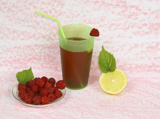 Малина на блюдце с лимоном и стакан сока на розовом фоне