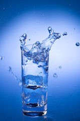 Mineral water splashing out from glass with ice cube.