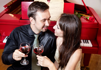 Couple with glasses of wine near piano