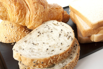 mixed bread, white bread and croissant on black tray.