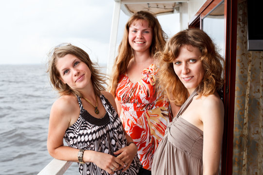 Three beautiful young women standing together on deck of yacht