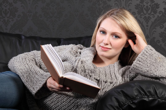 Smiling Blonde Woman Relaxing Reading Book At Home