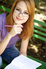Redhead girl in glasses doing homework at the park.