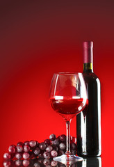 bottle of wine glasses and grapes on red background