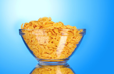 tasty cornflakes in glass bowl on blue background