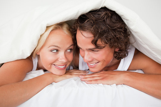 Couple under a duvet with a knowing smile