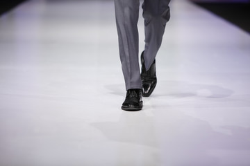 foot of male model in gray trousers and black shoes on catwalk