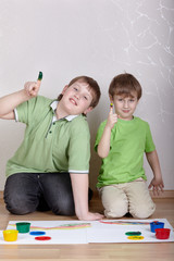 Naklejka premium Two boys in green T-shirts sit on floor and draw