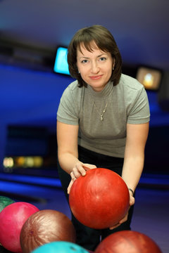 Woman takes  ball for playing in bowling and smiles