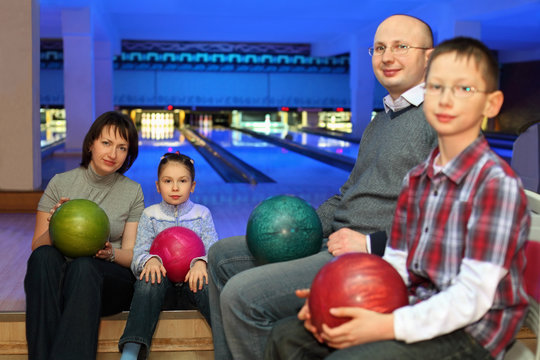 Family of four sit in club and hold balls for bowling