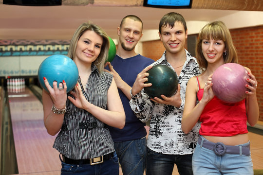 Two fellows and two girls stand in club, hold balls for bowling