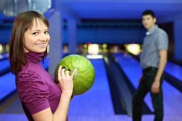 Fototapeta premium Girl holds ball for bowling and smiles, and man look at it