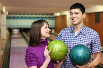 Fototapeta premium Young man and girl hold balls for bowling and laugh merrily