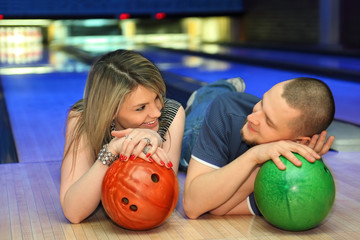 Fototapeta premium Couple lie on parquet, look on each other with balls for bowling